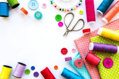 Beyaz arka planda aksesuar ve kumaş dikmek. Dikiş iplikleri, iğneler, iğneler, kumaşlar, düğmeler ve dikiş santimetresi. Üst manzara, düz uzanma.