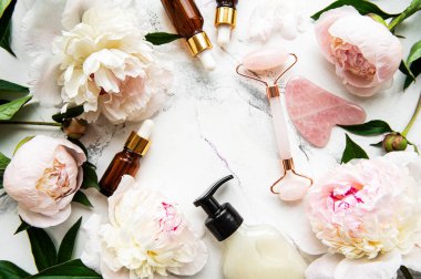 Yüz masajı terapisi, masaj yağları ve pembe şakayıklar için yeşim bir yüz silindiri. Düz beyaz mermer zemin üzerinde yatıyordu