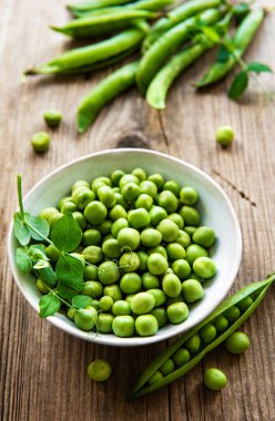 Beyaz kasede yeşil bezelyeler, ahşap masada taze kabuklar, üst ya da düz yatıyordu.