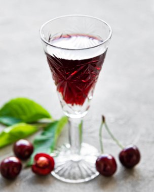 Bardakta kiraz likörü ve gri beton arka planda taze meyve.