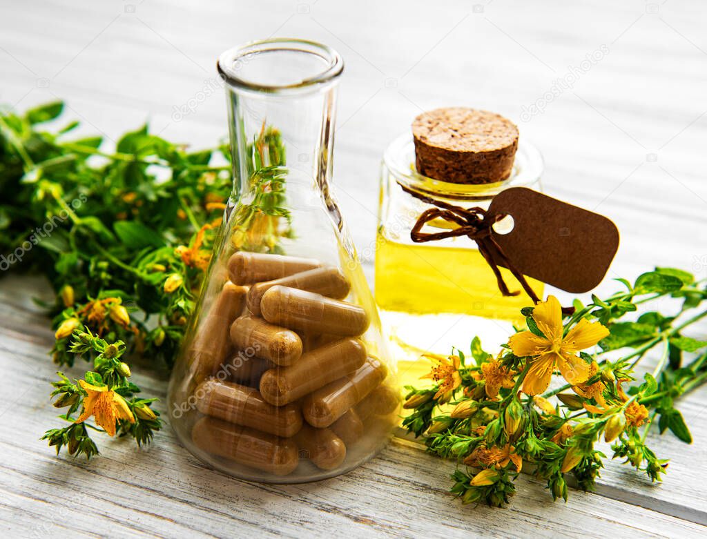 St. John's wort, herbal medical pills in test tube, bottles with natural oil on a table