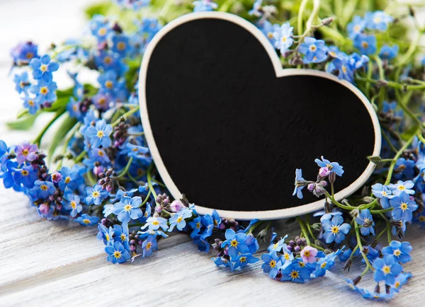 Forget-me-not flowers and black heart shaped board on white wooden background