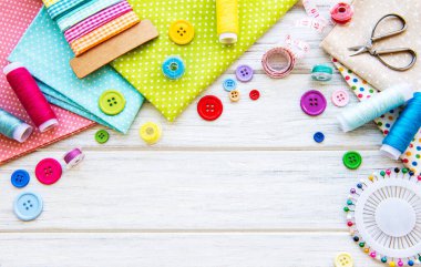 Beyaz arka planda aksesuar ve kumaş dikmek. Dikiş iplikleri, iğneler, iğneler, kumaşlar, düğmeler ve dikiş santimetresi. Üst manzara, düz uzanma.