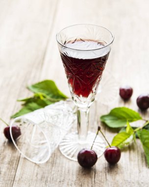 Bardakta kiraz likörü ve eski ahşap arka planda taze meyve.