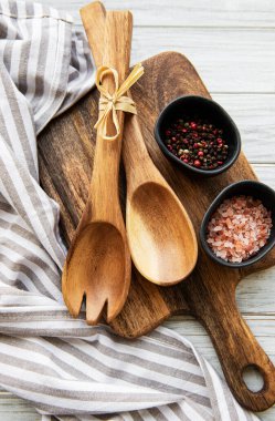 Eski mutfak gereçleri. Tahta kaşıklar, tahta kesme tahtası, beyaz ahşap masa üzerinde peçete ve baharatlar. Üst görünüm