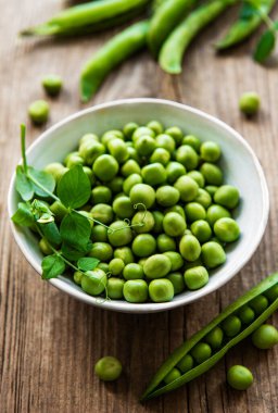 Beyaz kasede yeşil bezelyeler, ahşap masada taze kabuklar, üst ya da düz yatıyordu.