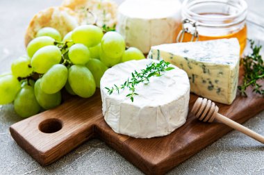 Gri beton arka planda peynir seçimi, bal ve üzüm