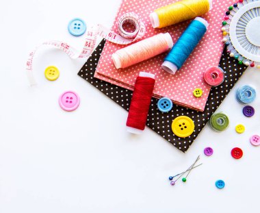 Beyaz arka planda aksesuar ve kumaş dikmek. Dikiş iplikleri, iğneler, iğneler, kumaşlar, düğmeler ve dikiş santimetresi. Üst manzara, düz uzanma.