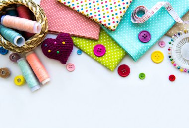 Beyaz arka planda aksesuar ve kumaş dikmek. Dikiş iplikleri, iğneler, iğneler, kumaşlar, düğmeler ve dikiş santimetresi. Üst manzara, düz uzanma.