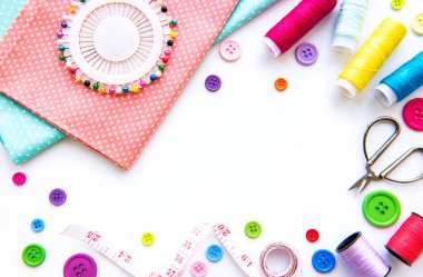 Beyaz arka planda aksesuar ve kumaş dikmek. Dikiş iplikleri, iğneler, iğneler, kumaşlar, düğmeler ve dikiş santimetresi. Üst manzara, düz uzanma.