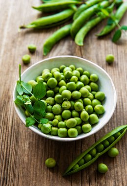 Beyaz kasede yeşil bezelyeler, ahşap masada taze kabuklar, üst ya da düz yatıyordu.