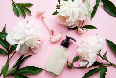 Yüz masajı terapisi, masaj yağları ve pembe şakayıklar için yeşim bir yüz silindiri. Pembe pastel arka planda düz uzandı