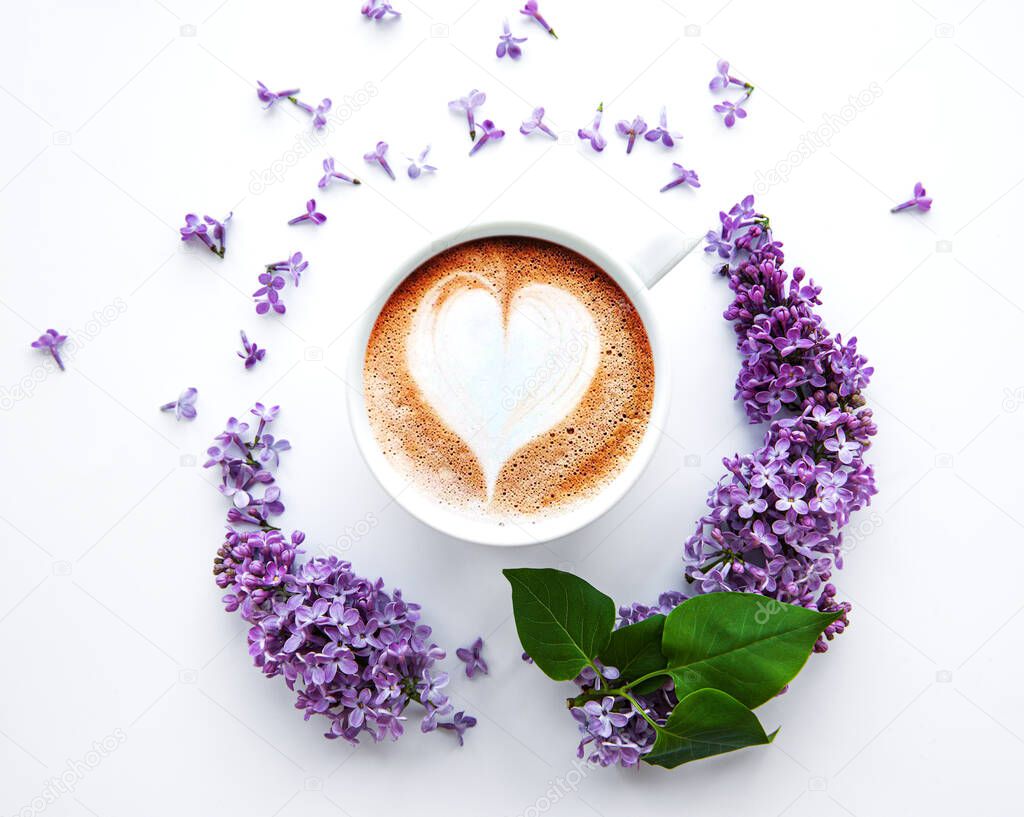 Lilac flowers on a white background in the shape of a circle top view on a cup of coffee