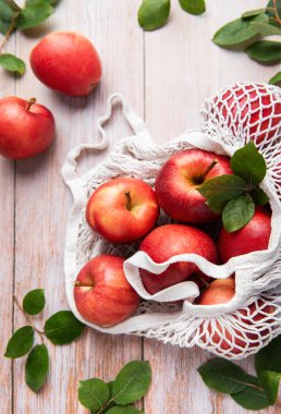 Yapraklı olgun kırmızı elmalar, yeniden kullanılabilir bir alışveriş çantasının içinde, tahta bir masada, sürdürülebilir bir yaşam tarzını sembolize ediyor.