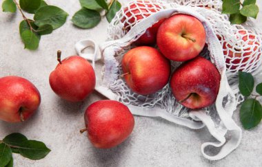 Olgun kırmızı elmalar yeniden kullanılabilir beyaz bir ağ torbasından dokulu bir yüzeye dökülüyor sağlıklı beslenmeyi ve sürdürülebilirliği teşvik ediyor.