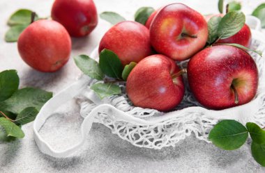 Olgun, yeşil yapraklı kırmızı elmalar sağlıklı beslenmeyi ve sürdürülebilirliği teşvik eden beyaz bir alışveriş torbasında otururlar.