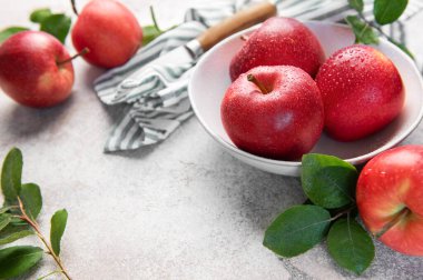 Olgun kırmızı elmalar ve su damlacıkları bir kasenin içinde, bir bıçak ve çizgili kumaşla birlikte, tüketilmeye hazır bekliyor.