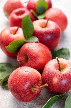 Yeşil yapraklı olgun kırmızı elmalar ve su damlacıkları taze ve sağlıklı bir imaj yaratıyor.