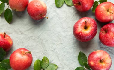 Olgun, yeşil yapraklı kırmızı elmalar gri keten arka planda canlı bir sergi sunan bir çerçeve oluşturur.