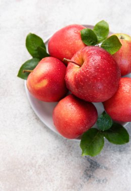 Su damlaları ve yeşil yapraklı olgun kırmızı elmalar, beyaz bir tabakta sıralanmış, taze ve sağlıklı bir görüntü yaratıyor.