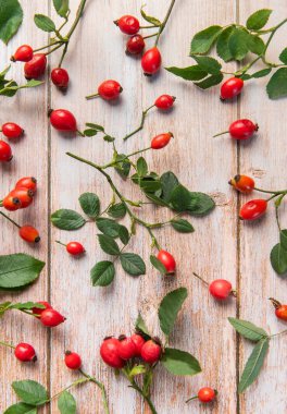 Rosehip böğürtlen ve yaprakları kırsal bir ahşap masa üzerinde canlı bir sonbahar görüntüsü oluşturuyor.
