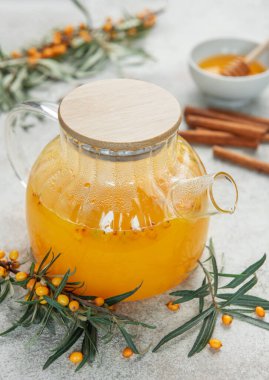 Cam çaydanlık, sıcak deniz dikenli çay, bal ve tarçın. Gri masaya çubuklar, üst manzara.