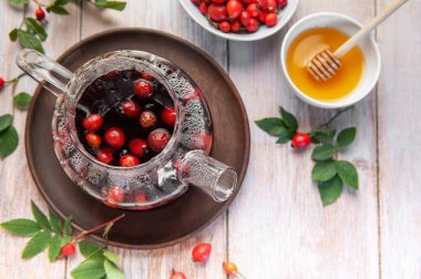 Bal ve taze gül kalçaları eşliğinde buğulanmış çay demleyen cam çaydanlık sağlıklı bir yaşam tarzını somutlaştırıyor.