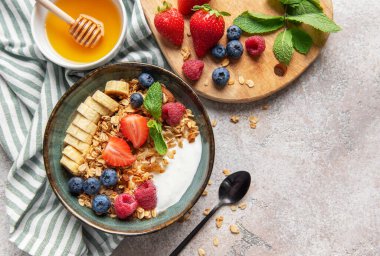 Yoğurtlu granola, muz, çilek, ahududu, yabanmersini ve bal sağlıklı bir kahvaltıdır.