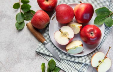 Olgun kırmızı elmalar, bütün ve dilimlenmiş, yeşil yapraklı beyaz bir tabakta, taze ve sağlıklı bir görüntü yaratıyor.