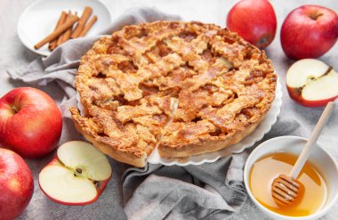 Taze elmalar, tarçın çubukları ve bal ile çevrili, bir dilim eksik ev yapımı elmalı turta.