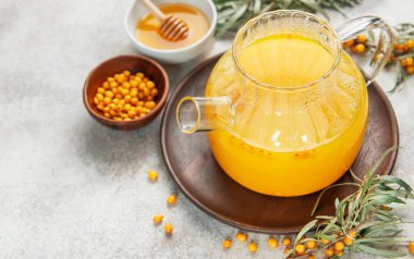 Sağlıklı bitkisel çayla dolu buharlı cam çaydanlığın yanında deniz dikenli çilek ve yapraklar.