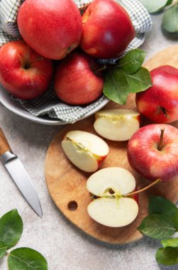 Fresh red apples, some sliced on a wooden cutting board, with a knife and a bowl of fruit