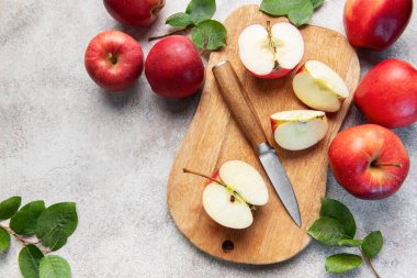 Olgun kırmızı elmalar, bütün ve dilimlenmiş, bir bıçakla ahşap bir kesme tahtasına yerleştirilmiş, kırsal ve sağlıklı bir mutfak sahnesi yaratıyor.