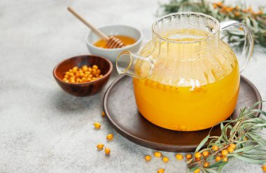 Sağlıklı bitkisel çayla dolu buharlı cam çaydanlığın yanında deniz dikenli çilek ve yapraklar.