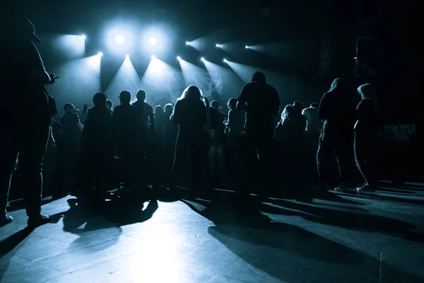Un grupo de personas esperando un concierto en un pequeño club en el fondo de un escenario con rayos de luz en la oscuridad — Foto de Stock