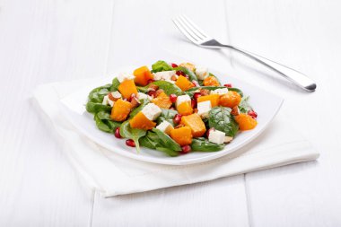 Salata ıspanak yaprakları, badem ve nar taneleri Beyaz ahşap masa üzerinde kabak ve beyaz peynir pişmiş. Sağlıklı gıda.