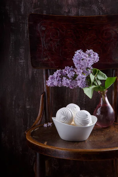 Bowl of white zephyr marshmallows and bouquet of lilac flowers o — Stock Photo, Image