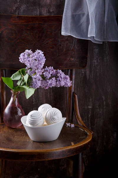 Bowl of white zephyr marshmallows and bouquet of lilac flowers o — Stock Photo, Image