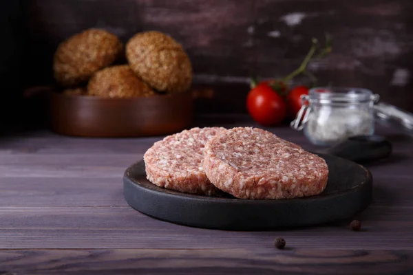 Chuletas de hamburguesas de carne picada cruda sobre fondo de madera oscura . — Foto de Stock