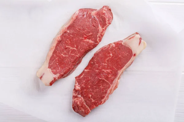 Το ακατέργαστο βόειο κρέας σε μπριζόλα. Δύο μπριζόλες λουρίδων με φιλέτο σε λευκό τραπέζι. — Φωτογραφία Αρχείου