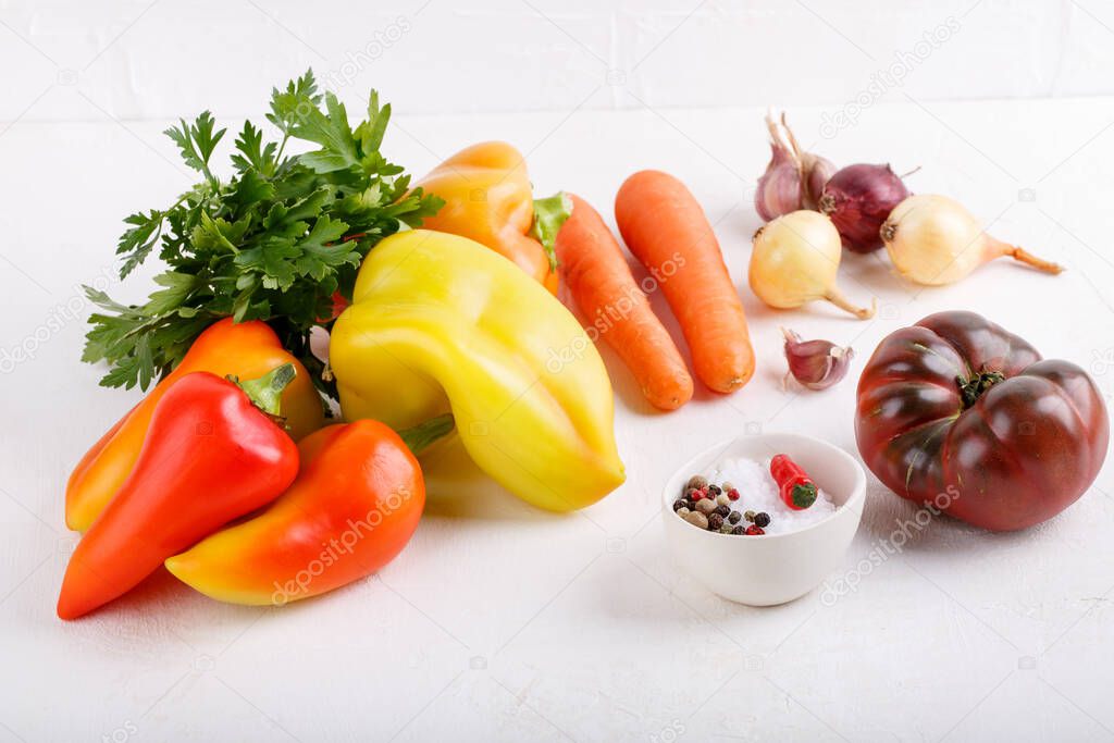 Ingredients for vegetable ragout on white table. Sweet pepper, carrot, onion, tomato, herbs and spice. Vegetarian food.