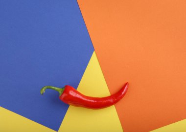 Çok renkli geometrik kağıdın arka planında kırmızı biber. Üst manzara, düz yatak, yakın çekim. Yiyecek konsepti.