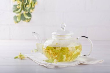 Şeffaf bir çaydanlıkta ıhlamur çayı. Beyaz arka planda bitkisel limon ağacı çayı olan cam çaydanlık. Şifalı bitki, bitkisel çaylar ve tentürler için kullanılan çiçekler..