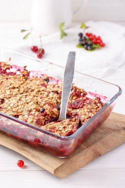 Elma ve böğürtlen ezmesi, üzerinde yulaf ve cam fırın kabıyla beyaz masada. Çıtır meyveli turta, sağlıklı yaz tatlısı. Yakın plan..