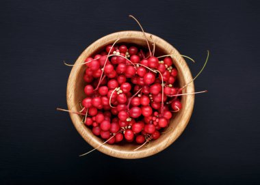Schisandra chinensis veya beş aromalı böğürtlen. Taze kırmızı olgun böğürtlenler, siyah arka planda ahşap kasede. Üst görünüm.