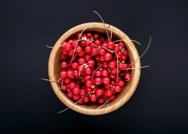 Schisandra chinensis or five-flavor berry. Fresh red ripe berries in wooden bowl on black background. Top view. clipart