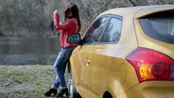 Una joven está de pie junto a un coche — Vídeos de Stock