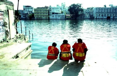 Geleneksel kırmızı ve sarı kostümlü üç adam gölün kenarında oturuyor.