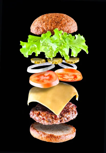 Delicious tasty hamburger with flying ingredients isolated on black background. Burger parts flying in air. Floating Burger