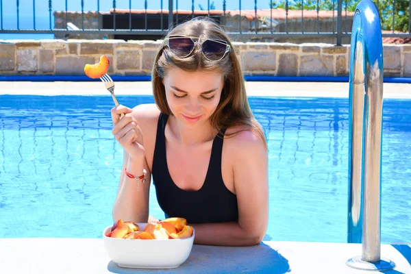 Krásná mladá žena jíst ovoce u bazénu, koncept dovolenou zdravého životního stylu — Stock fotografie